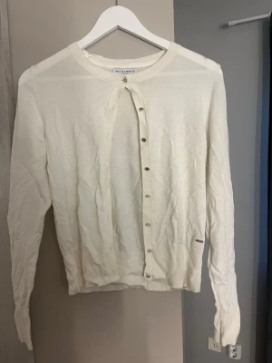 Vit kofta/Sweter rozpinany - Klassisk vit kofta från Holly & Whyte by Lindex med rund halsringning och guld knappar framtill. Långärmad modell i mjukt, tunt material som passar perfekt till lager på lager. Stilren och enkel design med ribbade muddar.