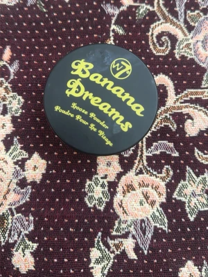 W7 Banana Dreams Loose Powder - Banana Dreams Loose Powder från W7 är ett löspuder i en rund svart burk med gul text. Pudret har en ljusgul ton som ger en matt finish och är perfekt för att fixera foundation och highlighta ansiktet. Passar för dig som vill ha en naturlig och fräsch look. Bara test af e!