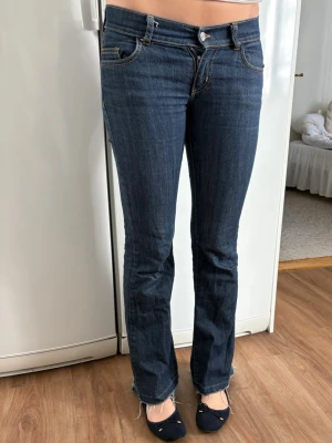 Mörkblå bootcut jeans, tall. - Mörkblå bootcut jeans med låg midja och klassiska fem fickor. Märke: Carmar Los Angeles. Jeansen har kontrastsömmar och råa kanter vid bensluten för en cool look. Jeansen är långa, tjejen på bilden är 178 cm lång. Spettade o sydda längs ner. Se bild. Perfekta för dig som gillar en tidlös och avslappnad stil.