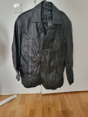 Svart skinnjacka med klassisk krage - Stilren svart skinnjacka från Mile med klassisk krage och knäppning framtill. Jackan har raka linjer, diskreta sömmar och en tidlös design som passar till många olika stilar. Perfekt för dig som gillar en clean look.