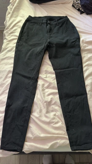 Svarta chinos med smal passform (L/XL) - Snygga svarta chinos med smal passform och klassiska fickor. Byxorna har bälteshällor och stängs med knapp och dragkedja. Perfekta för en stilren look och lätta att matcha med olika outfits.