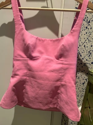 Rosa Zara topp med rosett och öppen rygg - Supersöt rosa linnetopp med breda axelband och en rosett bak samt öppen rygg. Toppen har figurnära passform och lätt utsvängd nederkant. Perfekt för dig som vill sticka ut med en färgglad och trendig look.
