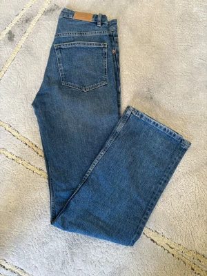 Blå raka jeans från Gina Tricot - Klassiska blå jeans från Weekday med rak passform och fem fickor. Jeansen har normal midja, bälteshällor och är tillverkade i denim av bomull. Perfekta för en avslappnad och stilren look.