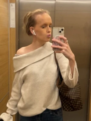 Off shoulder beige stickad tröja - Trendig off shoulder stickad tröja i vit färg. Tröjan har en avslappnad passform med långa ärmar och ribbade muddar. Perfekt för en stilren och modern look.