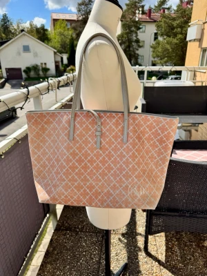 Väska från By Malene Birger - Stilren väska i beige/rosa och vitt med By Malene Birgers klassiska mönster. Väskan har långa, smala handtag i ljusgrått. Den är lite sliten på utsidan, mest den sidan mot kroppen, därav priset. Se bilderna 🌸