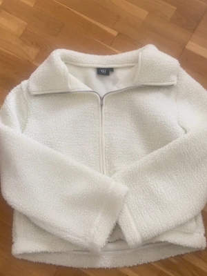 Vit teddyjacka från 157 - Supermjuk och fluffig vit teddyjacka från 157 med dragkedja framtill och hög krage. Jackan har en klassisk rak passform och är gjord i ett mysigt teddy-material.🩷