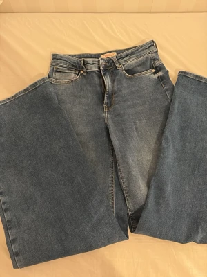 Blå raka jeans från ONLY - Säljer ett par klassiska blå jeans från ONLY med rak passform och hög midja. Jeansen har fem fickor, bälteshällor och stängs med knapp och dragkedja. Tillverkade i slitstark denim som ger en tidlös look.