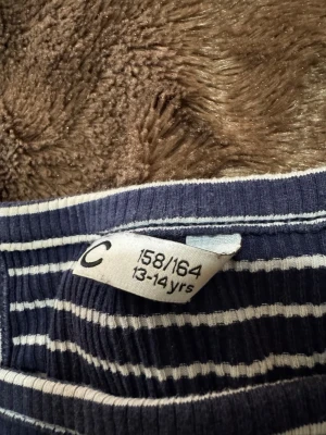 Randig blå linnetopp - Snygg ribbad linnetopp i marinblått med vita ränder. Toppen har ärmlös design och smala axelband, perfekt för en avslappnad stil. Passar dig som gillar sportig och enkel look.