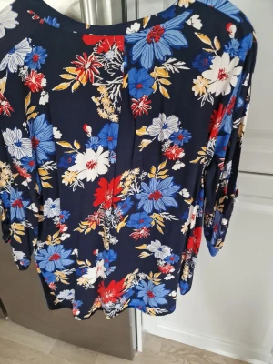 Blommig blus i marinblått - Snygg blus med färgglatt blommönster i blått, rött, vitt och gult på marinblå botten. Storlek Xl men lite osäkert.