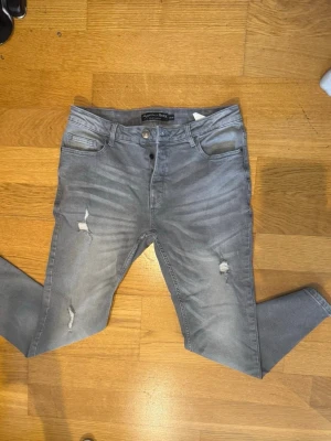 Grå slim fitt jeans med slitningar (Amaci ’sons) W33 L30 - Säljer ett par grå skinny jeans från Amaci ’Sons  med slitningar på låren och knäna. Jeansen har fem fickor, och stretchigt material för skön passform. Perfekta för en avslappnad och trendig look. W32 L30