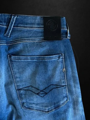  Replay Anbass - Snygga blå jeans från Replay med klassisk femficksdesign och diskret broderi på bakfickan. Jeansen har en rak passform och är tillverkade i stretchigt denim för extra komfort. Perfekta för en avslappnad och trendig look.