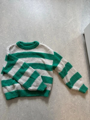 Grön- och vitrandig stickad tröja - Stickad tröja med breda gröna och vita ränder, rund halsringning och ribbstickade muddar vid ärmslut och nederkant. Tröjan har en avslappnad passform och är perfekt för lager-på-lager-stil. Materialet känns mjukt och mysigt. Inte alls stickigt (från någon som hatar känslan av stick)