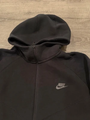 Svart Nike zip hoodie med huva - Snygg svart hoodie från Nike med dragkedja framtill och två fickor med dragkedja. Klassisk Nike-logga på bröstet och skön huva. Perfekt för en avslappnad streetwear-look. Tillverkad i mjukt material som känns bekvämt hela dagen.