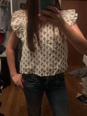 Vit blus med volangärmar och mönster - Supersöt vit blus med svarta grafiska mönster och stora volangiga korta ärmar. Aldrig använt!  