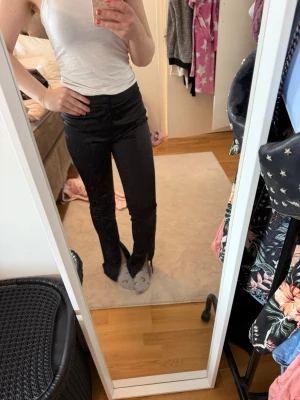 Svarta slitsbyxor med hög midja - Snygga svarta byxor med hög midja och slits framtill vid bensluten. Byxorna har en tight passform upptill och är raka nedtill, vilket ger en trendig look. Perfekta att styla med sneakers eller klackar. Materialet känns mjukt och stretchigt.