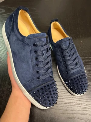 Mörkblå sneakers med nitar - Snygga mörkblå sneakers i mocka från Christian Louboutin med coola svarta nitar på tån. Skorna har vita sulor, matchande mörkblå skosnören och en klassisk låg modell. Perfekta för dig som vill sticka ut med en edgy och lyxig stil.