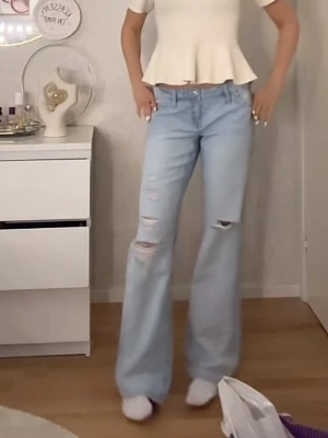 Ljusblå slitna bootcut jeans - Säljer ett par ljusblå bootcut jeans med slitningar och hål på båda benen. Från Gina 14+!