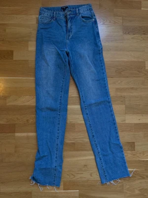 Blå raka jeans med slitet benslut PLT  - Säljer ett par klassiska blå jeans från Pretty Little Thing TALL med hög midja och raka ben. Jeansen har fem fickor och råa, fransiga benslut för en trendig look. Perfekta till sneakers eller boots. Materialet är 100% bomull för en skön känsla.
