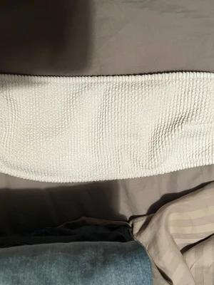 Vit ribbad bandeau bad tubtopp - Säljer en vit bandeau bad tubtopp med ribbad struktur. Toppen är ärmlös och har en enkel, stilren design som passar perfekt till många olika outfits.