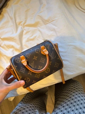 Louis Vuitton monogram handväska - Snygg handväska från Louis Vuitton i klassiskt brunt monogrammönster med ljusbruna läderdetaljer och guldfärgade metalldetaljer. Väskan har både handtag och axelrem, perfekt för dig som gillar lyxiga accessoarer och tidlös design. Kom med prisförslag säljer endast vid bra då jag inte e säker på om jag vill sälja