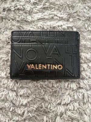 Svart Valentino kortfodral i läder - Snyggt svart kortfodral från Valentino i läder med präglad logotyp över hela ytan och guldfärgad VALENTINO-text framtill. Perfekt för kort och ID, stilren och smidig att ha i fickan.