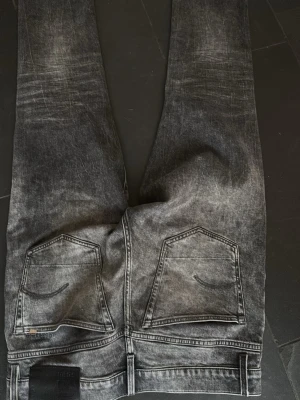 Grå slim fit jeans  - Säljer ett par grå slim fit jeans från G star rawmed snyggt tvättad look och klassiska fem fickor. Jeansen har raka ben och svart läderpatch bak i midjan. Perfekta för dig som gillar en modern och avslappnad stil.32/34
