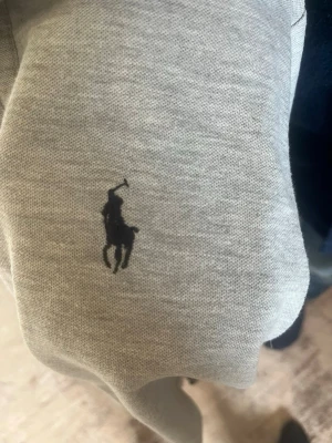 Grå t-shirt från Ralph Lauren - Snygg grå piké från Ralph Lauren med klassisk svart polologga broderad på bröstet. Pikén är i mjuk bomull och har en enkel, stilren design som passar till allt. Perfekt för dig som gillar Avslappnad och clean stil.