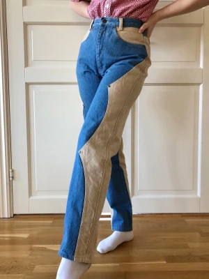 Retro Western jeans - Unika jeans med effektfull design skapad med denim tyg i två olika nyanser. Framsidan har en vågig söm försedd med nitar och baksidan har ett v-format ok. Sitter som en smäck på någon med kurvig figur. Högmidjade med avsmalnande ben. Stora framfickor, gylf och hällor. Fantastiska detaljer såsom nitar med inristningar, knapp med logga och hälla med broderad logga. Materialet är kraftigt och kvalitén rejäl. Utmärkt skick!  Från Quarterhorse, USA, troligtvis är byxorna tillverkade på 80-talet. 