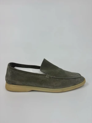 Grå Loro Piana mockaloafers med beige sula - Stilrena loafers i grå mocka med klassisk design och låg beige gummisula. Skorna har en enkel slip-on-modell utan snörning och en mjuk ovandel i mocka som ger en avslappnad men snygg look.