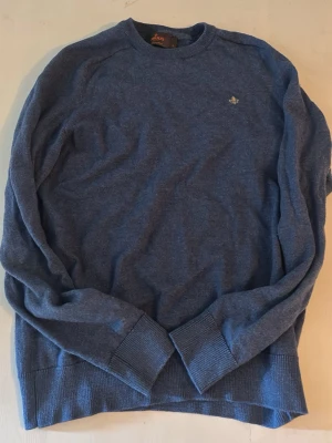 Blå stickad tröja från Morris - Mysig blå stickad tröja från Morris med rund halsringning och diskret broderad logga på bröstet. Tröjan har långa ärmar och ribbade muddar vid ärmslut och nederkant. Perfekt för lager-på-lager och enkel att matcha.