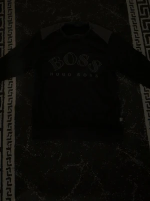 Svart sweatshirt från Hugo Boss - Cool svart sweatshirt från Hugo Boss med stor BOSS-logga framtill. Tröjan har rund halsringning och kontrastpaneler vid axlarna. Perfekt för en avslappnad och stilren look.