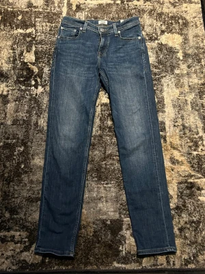 Blå raka jeans från Jack & Jones - Snygga blå jeans från Jack & Jones med klassisk rak passform och fem fickor. Jeansen har tydliga kontrastsömmar och är gjorda i denim med en lätt tvättad look. Perfekta för en avslappnad och stilren outfit.