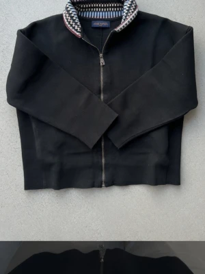 Louis Vuitton Zip Jacket  - Snygg Louis Vuitton zip-up jacka i mörkblå färg med ikonisk mönstrad krage i LV-stil. Storlek: M (Medium) Skick: Ny utan prislapp – har bara legat i garderoben, aldrig använd. Perfekt skick! Jackan har en fin passform, hög kvalitet och den klassiska Louis Vuitton-loggan på dragkedjan. Mönstrad insida på kragen ger en lyxig detalj. Kommer från djurfritt och rökfritt hem. Packas säkert och noga.