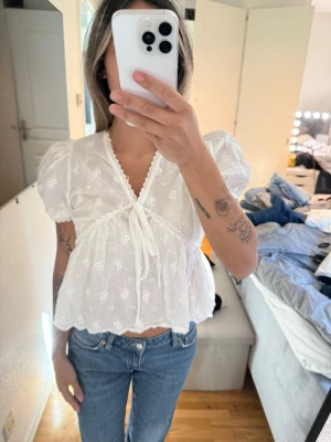 Vit blus med spets och puffärm - Söt vit blus med kort puffärm, v-ringning och knyt framtill. Blusen har broderade spetsdetaljer och volangkant nertill. Perfekt för en trendig och romantisk look. Står ingen storlek men passa mig som bruka ha xs-S