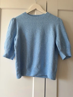 Ljusblå stickad tröja Vero Moda - Ljusblå stickad tröja från Vero Moda med rund halsringning och halvlånga puffärmar. Tröjan har ribbade muddar vid hals, ärmslut och nederkant. Perfekt för dig som gillar en enkel men söt look.