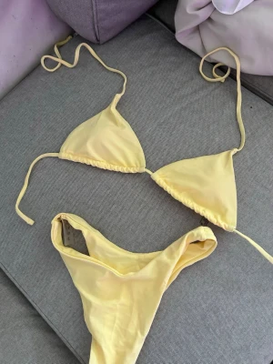 Gul triangelbikini med knyt - Snygg gul bikini med klassisk triangelmodell och knyt i sidorna och nacken. Bikinin har en enkel och stilren design, perfekt för stranddagar. Materialet känns mjukt och följsamt mot huden.