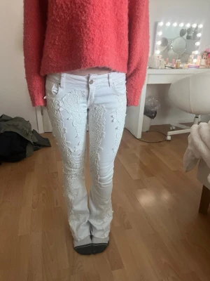 Vita bootcut jeans med spetsdetaljer - Säljer ett par vita bootcut jeans med snygga broderade spetsdetaljer framtill. Jeansen har låg midja, klassiska fickor och stängs med knapp och dragkedja. Perfekta för dig som vill sticka ut med en unik look. Dem har två fläckar som bara syns i vissa ljus (skriv om ni vill ha bild), dom är hyfsat stretchiga och lågmidjade. Priset kan diskuteras, bara att skriva om ni undrar något!☺️