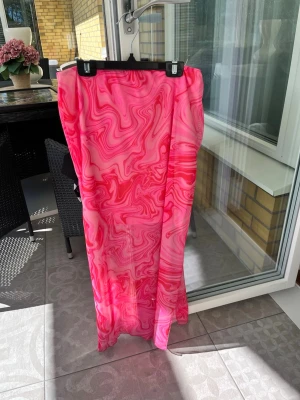 Långkjol med rosa mönster - Säljer en långkjol med swirlmönster i olika nyanser av rosa och rött. Kjolen är i ett tunt, flowy material som ger en snygg och luftig känsla. Perfekt för dig som vill sticka ut med färg och mönster.