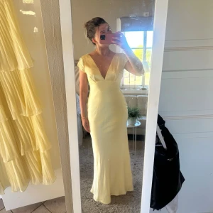Hello Molly Balklänning Ljusgul med v-ringning - Populär klänning från Hello Molly, slutsåld på hemsidan och svår att få tag i. Elegant ljusgul långklänning med djup v-ringning fram och öppen rygg. Klänningen har korta ärmar och figurnär passform. Perfekt för bal. Prislapp är kvar och skickas i samma påse den kom i💓💓