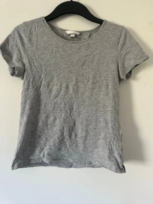 Grå basic t-shirt i bomull - En enkel och stilren grå t-shirt med rund halsringning och korta ärmar. Perfekt för en avslappnad look och lätt att matcha med andra plagg. Tillverkad i mjuk bomull för skön komfort.