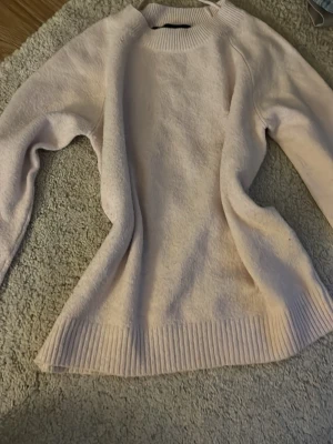 Ljusrosa stickad tröja - Mysig ljusrosa stickad tröja med rund halsringning och ribbade muddar vid ärmslut och nederkant. Perfekt för kyliga dagar och enkel att matcha med jeans eller kjol. Tröjan har en avslappnad passform och är tillverkad i mjukt material.