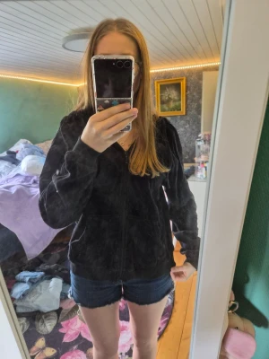 Svart hoodie med dragkedja - Svart hoodie med dragkedja framtill och två fickor. Klassisk modell med huva och ribbade muddar vid ärmslut och nederkant. Perfekt för en avslappnad stil och enkel att matcha med andra plagg.