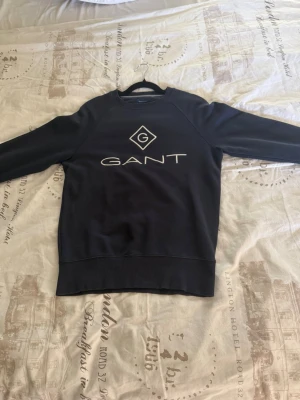 Mörkblå sweatshirt från GANT - Stilren svart sweatshirt från GANT med stor vit logga på bröstet. Kan användas till finare tillfällen men även till en vardaglig använding. Storleken är Xs så om du behöver nått till ditt barn hade denna tröjan varit perfekt