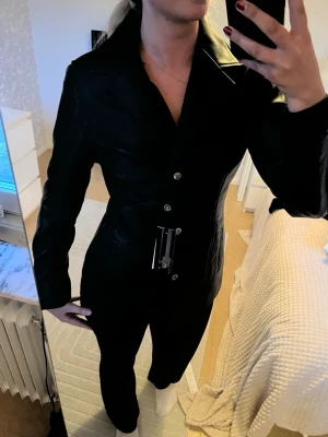 Svart skinnjacka med bälte - Snygg svart skinnjacka med markerad midja - figursydd. Jackan har klassisk krage, knäppning framtill och en stilren, figurnära passform. Älta läder, aldrig använd helt ny med prislapp från AC Made in Italy
