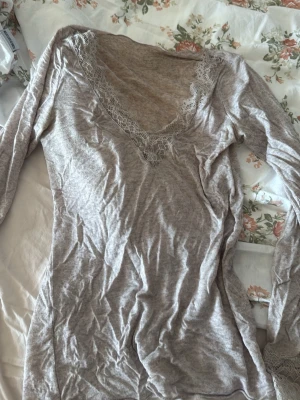 Beige långärmad loungewear topp - Mysig beige långärmad topp i mjukt material, perfekt för hemmakvällar. Djup V-ringning med spetsdetaljer runt halsen ger en feminin touch. Tunn och stretchig kvalitet som känns skön mot huden.