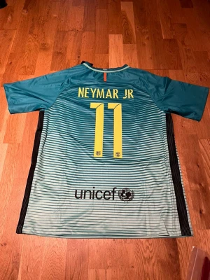 Barcelona third kit Neymar jr #11 - Snygg FC Barcelona matchtröja i turkos med svarta och vita ränder, Neymar Jr och nummer 11 på ryggen. Nike-logga och klubbmärke på bröstet, samt Qatar Airways och UNICEF-tryck. Perfekt för fotbollsfans!
