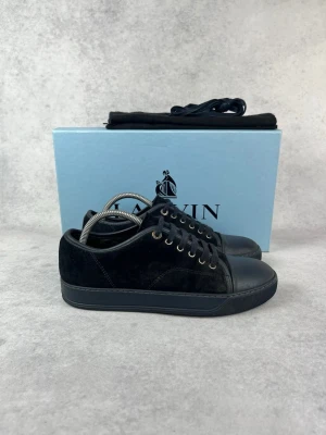 Svarta sneakers från Lanvin i mocka - Stilrena svarta sneakers från Lanvin med ovandel i mjuk mocka och tåparti i slätt läder. Skorna har svarta skosnören, metallfärgade öljetter och en svart gummisula. Perfekta för dig som gillar en clean och lyxig look.