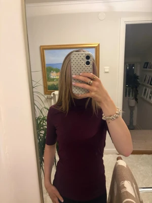 Vinröd polotopp från Pieces - Säljer en vinröd polotopp från Pieces i storlek S. Toppen har halvlånga ärmar och en hög polokrage. Materialet är mjukt och stretchigt, vilket gör den riktigt skön att bära. Perfekt att styla med jeans eller kjol för en clean look.