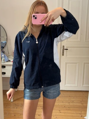 Nike jacka - Snygg mörkblå vindjacka från Nike med vita detaljer på sidorna. Jättefint skick, inga skador eller så. Barnstorlek med passar mig som brukar ha xs💕