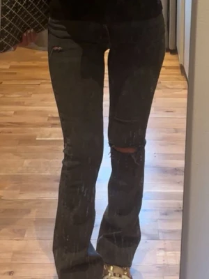 Svarta bootcut jeans med slitningar - Snygga svarta bootcut jeans med slitningar på knäna och lätt utsvängda ben. Jeansen har en klassisk femficksmodell och låg midja. Perfekta för en trendig och avslappnad stil.storlek 32